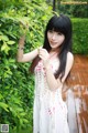 A woman in a white dress standing next to a bush.