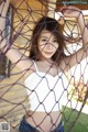 A woman in a white top and blue jeans posing behind a net.