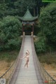 A naked woman standing on a wooden bridge in the woods.