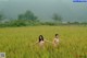 Two naked women walking through a field of tall grass.