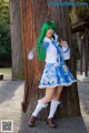 A woman with green hair standing next to a tree.