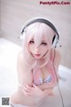 A woman with pink hair wearing headphones in a bathtub.