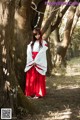 A woman in a red and white kimono standing next to a tree.