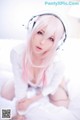 A woman with pink hair wearing headphones on a bed.