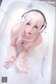 A woman with pink hair and headphones in a bathtub.