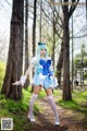 A woman in a blue and white dress is standing in the woods.