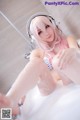 A woman with pink hair sitting in a bathtub with headphones on.