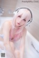 A woman with pink hair sitting in a bathtub with headphones on.