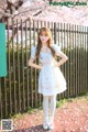 A woman in a white dress standing in front of a fence.