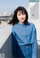 A woman in a blue shirt and jeans leaning against a wall.