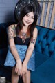 A woman sitting on a blue couch with tattoos on her arms.