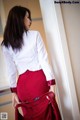 A woman in a white shirt and red skirt leaning against a wall.