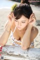 A woman in a bikini sitting on a bench on the beach.