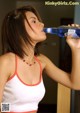 A woman in a white tank top drinking from a bottle.