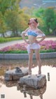 A woman in a bikini standing on a rock by a pond.