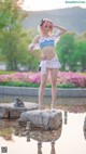 A woman in a bikini standing on a rock by a pond.