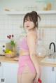 A woman in a pink top and skirt standing in a kitchen.