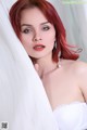 A woman with red hair wearing a white bra and earrings.