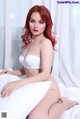 A woman with red hair sitting on a bed.