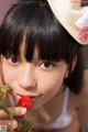 A young girl in a straw hat holding a strawberry.