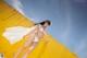 A woman in a white bikini standing in front of a yellow wall.