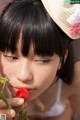 A young girl in a straw hat eating a strawberry.