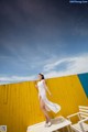 A woman in a white dress standing on a wooden bench.