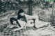 Two naked women laying on a blanket in the woods.