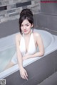 A woman in a white dress sitting in a bathtub.