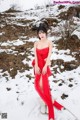 A woman in a red dress is posing in the snow.