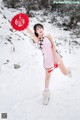 A woman in a pink dress holding a red fan in the snow.