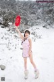 A woman in a pink dress holding a red fan in the snow.