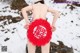 A woman in a bikini holding a red paper cutout in the snow.