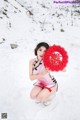 A woman in a pink dress holding a red fan in the snow.