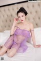 A woman in a purple lingerie sitting on a bed.