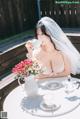 A woman in a wedding dress sitting at a table with a cup of coffee.