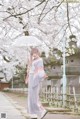 A woman in a kimono holding an umbrella in front of a tree.