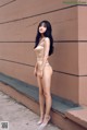 A woman in a nude bodysuit leaning against a wall.