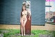 A naked woman standing next to a large metal sculpture.