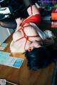 A woman in a red and white shirt is tied up on a desk.