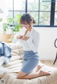 A woman in a white shirt and blue skirt sitting on a couch.