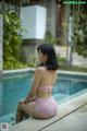 A woman in a pink bikini sitting by a swimming pool.