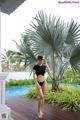 A woman in a black bikini standing next to a pool.