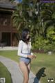 A woman in a white top and blue shorts walking down a sidewalk.