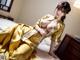 A woman in a yellow kimono sitting on a bed.