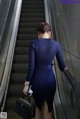 A woman in a blue dress is walking down an escalator.