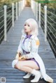 A woman in a white coat and purple skirt sitting on a wooden bridge.