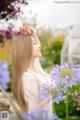 A woman with long blonde hair standing in a field of flowers.