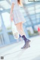 A woman walking down a sidewalk carrying a plastic bag.