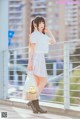 A woman in a white shirt and plaid skirt holding a shopping bag.